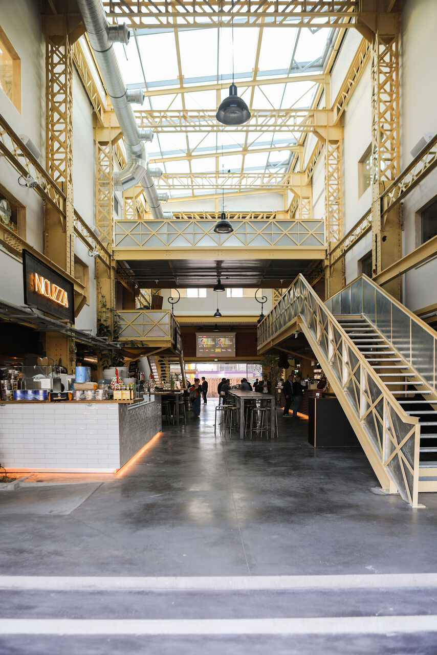 Aménagement intérieur du foodcourt Atelier des Citernes à Bordeaux avec structure métallique conservée